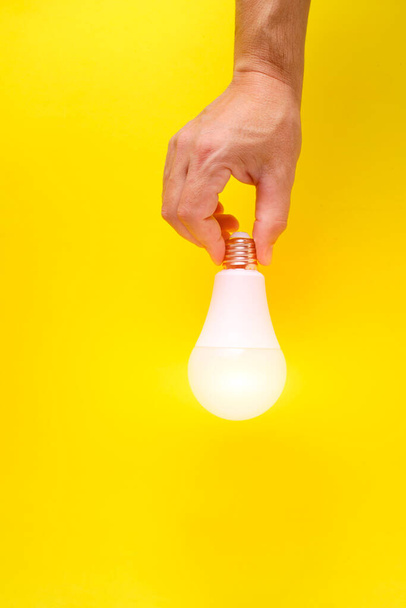 LED eco friendly light bulb in hand on yellow background - Fotoğraf, Görsel