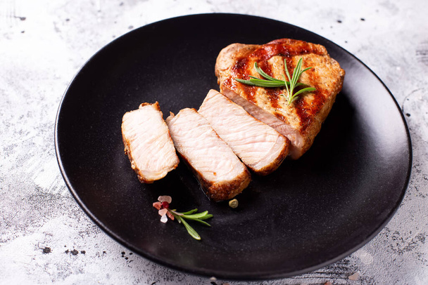 Sliced  grilled pork steak with spices and rosemary on black plate on grey textured background.  - Фото, изображение