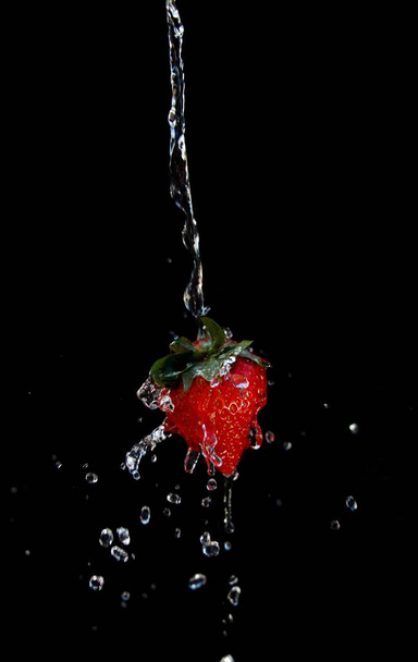 red strawberries being doused with plenty of water against a black background - Foto, Bild