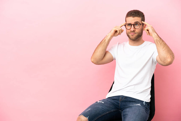 Young man sitting on a chair over isolated pink background having doubts and thinking - Foto, Bild