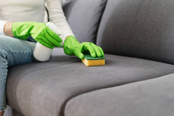 vágott lövés női kéz zöld gumikesztyűben mosás kanapé kárpit szivaccsal és mosószer spray a nappaliban a modern lakás, házimunka koncepció - Fotó, kép