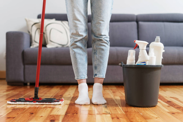 balde de plástico com produtos detergentes e fêmea com esfregão vermelho para lavar o chão na sala de estar no apartamento moderno, tiro cortado, conceito de tarefas domésticas - Foto, Imagem