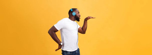 Jeune homme afro-américain portant un casque et profiter de la musique dansant sur or jaune Fond
. - Photo, image