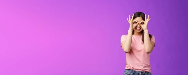 Cheerful friendly carefree asian woman having fun fool around, show okay ok signs on eyes make glasses from fingers, smiling delighted, mimicking funny emotions, stand purple background happy. - Photo, Image
