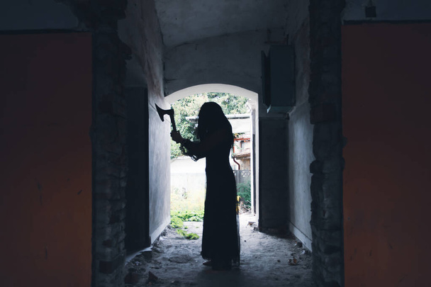 Ghost in abandoned, haunted house. Horror scene of spooky silhouette holding old axe, halloween concept. - Photo, Image