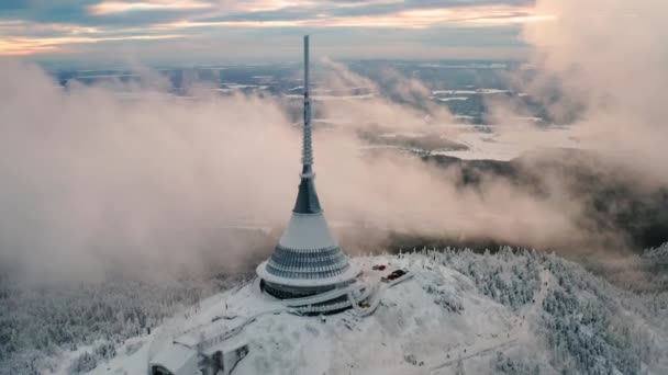 Torre de broma construida en lo alto de la montaña forestal cubierta de nieve. Alta construcción con diseño futurista y aguja afilada en vista aérea de neblina - Metraje, vídeo
