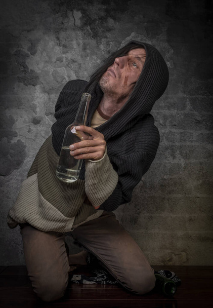 Homem de cabelo preto com garrafa de álcool perto de parede de tijolo velho - Foto, Imagem