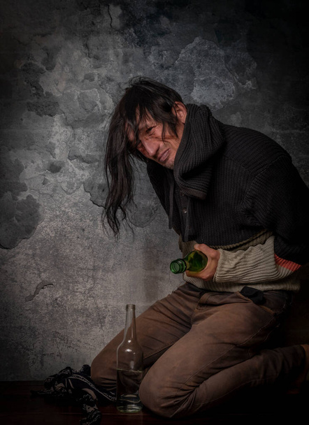 Homme aux cheveux noirs avec bouteille d'alcool près d'un vieux mur de briques - Photo, image