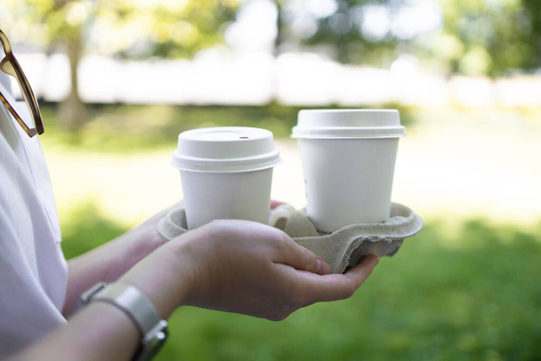 Mujer manos de mujer sosteniendo dos tazas de papel de café caliente en el parque de verano de la ciudad. - Foto, imagen