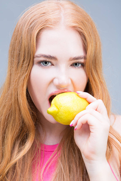 Young beautiful woman eating lemon isolated on gray background. Healthy eating concept. Diet. - Photo, image
