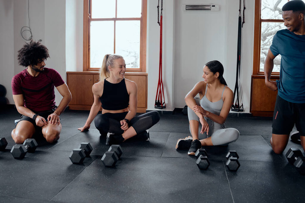 Group of confident multiracial young adults in sportswear sitting by weights at the gym - Photo, Image