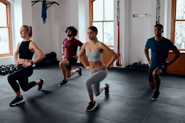 Group of multiracial young adults in sportswear doing lunges with hands on hips at the gym - Foto, afbeelding