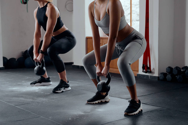 Young caucasian woman and biracial woman in sportswear doing kettlebell squats at the gym - Fotoğraf, Görsel
