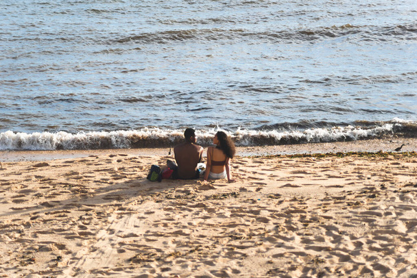 Salvador, Bahia, Brazil - December 12, 2021: A man and a woman sitting on the beach sand outdoors. Beautiful sunny day. City of Salvador, Brazil. - 写真・画像