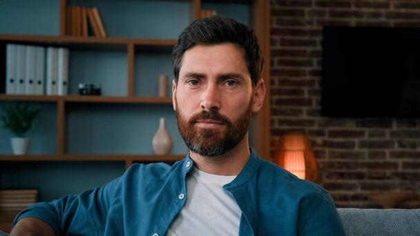 Head shot handsome bearded caucasian guy confident serious 30s male portrait wears casual blue shirt attractive caucasian man homeowner client sit on sofa at home looking at camera with serene emotion - Photo, Image