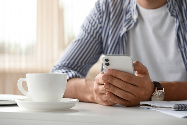 Man sitting at table and using smartphone in room, closeup - Foto, imagen