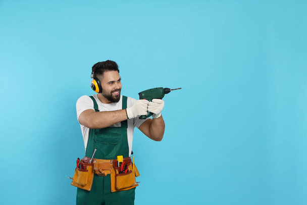 Young worker in uniform with power drill on light blue background. Space for text - Foto, imagen