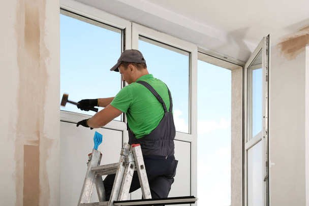 Worker on folding ladder installing window indoors - 写真・画像