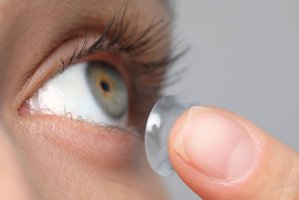 Woman putting in contact lens on grey background, closeup view - Foto, immagini