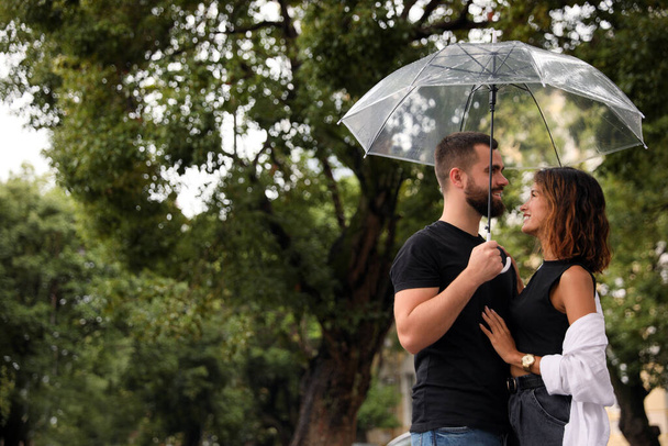 Young couple with umbrella enjoying time together under rain outdoors, space for text - Foto, Bild