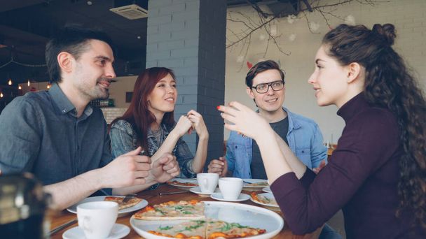 Amigos cercanos están compartiendo historias divertidas haciendo gestos y riéndose mientras almuerzan en la moderna cafetería local. Emociones positivas, gente feliz y sabroso concepto de comida
. - Foto, Imagen