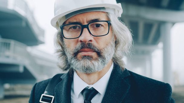 Close-upportrait of building project manager wearing formal clothing and helmet standing outdoors in construction site. People and career concept. - Фото, зображення
