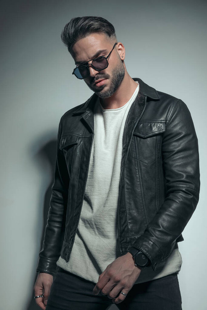cool fashion model looking down, wearing sunglasses and a leather jacket with masculine frame  - Photo, Image