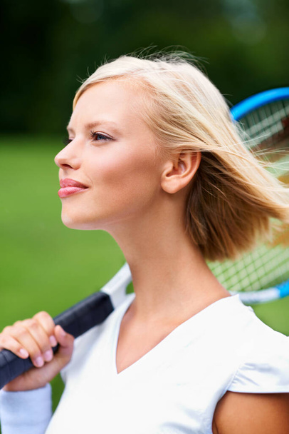 Dává pozor na míček. Mladá tenistka s větrem ve vlasech a raketou na rameni - Fotografie, Obrázek