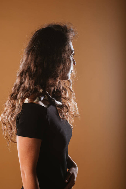 Gyönyörű lány göndör haj pózol egy fekete-fehér kígyó a stúdióban egy sárga háttér - Fotó, kép