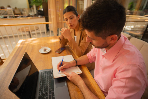 Hombre de negocios escribiendo notas sobre su proyecto de negocio con su colega mientras toma un café en una tarde soleada - Foto, imagen