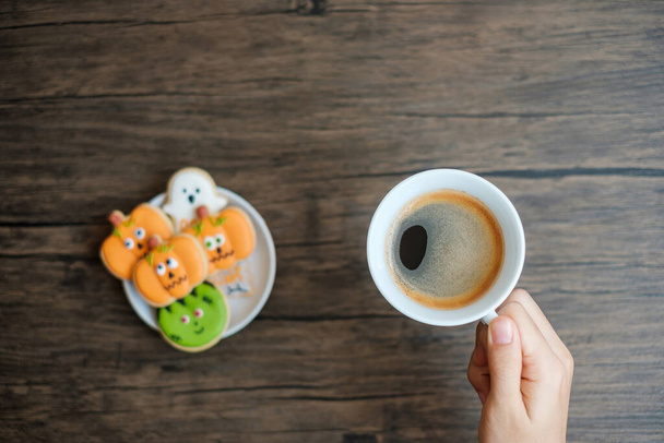 mão segurando xícara de café durante comer biscoitos de Halloween engraçado. Feliz Dia das Bruxas, Truque ou Ameaça, Olá Outubro, outono outono, Tradicional, festa e conceito de feriado - Foto, Imagem