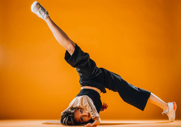 Fit young girl dancer performing a dance routine in the orange studio - Fotó, kép