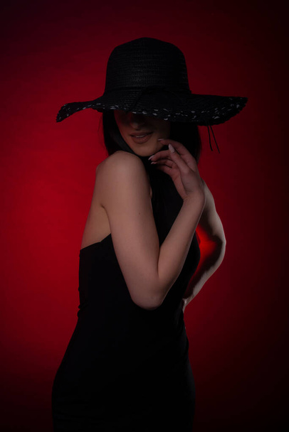 Elegante meisje in zwart jurk is poseren op rode achtergrond in studio - Foto, afbeelding