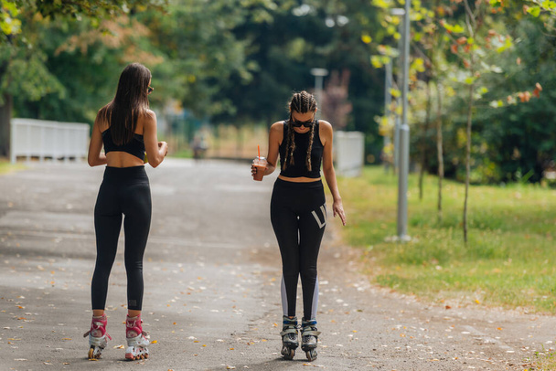 Duas mulheres em sportswear patinagem no parque em tempo ensolarado. - Foto, Imagem