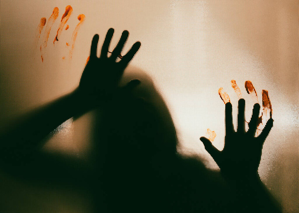 Horror ghost woman with blooded hands behind the matte glass. Halloween festival concept. - 写真・画像