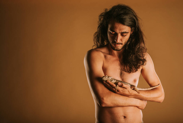 Handsome man looking and holding his pet bearded dragon at the studio - Photo, Image