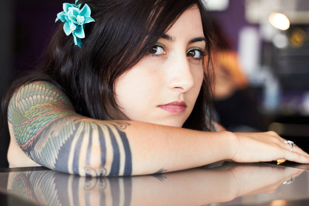 Εκφράζει την ταυτότητά της μέσω της τέχνης. Μια νεαρή καλλιτέχνιδα τατουάζ επιδεικνύει το τατουάζ στο μανίκι της ενώ ακουμπάει το κεφάλι της στο χέρι της. - Φωτογραφία, εικόνα