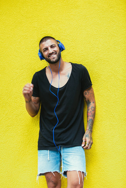 Tattoo man écoute de la musique à l'aide d'écouteurs sur un mur jaune - Photo, image