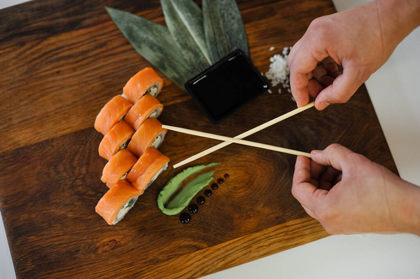 close-up van heerlijke sushi met stokjes en zalm op houten snijplank - Foto, afbeelding