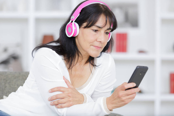 mature woman listening to audio and carrying phone - Φωτογραφία, εικόνα