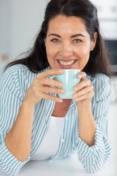 lovely middle-aged woman with a beaming smile holding a coffee - Photo, image