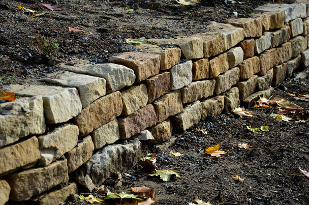 Die Trockenmauer dient als Terrassenterrasse für den Garten, wo sie eine Masse Erde hält. Die Wand ist leicht gewölbt, wodurch sie sich besser stabilisiert. Pflanzen von Stauden und Steingärten, Kies - Foto, Bild