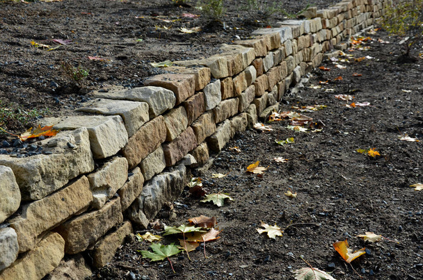 Сухая стена служит террасой для сада, где она удерживает массу почвы. Стена слегка изогнута, что помогает ей лучше стабилизироваться. посадка многолетних и скальных садов, гравия - Фото, изображение