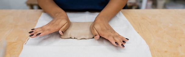 vista cortada da mulher americana africana em avental pressionando pedaço de argila com as mãos durante a classe cerâmica, banner - Foto, Imagem
