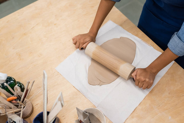 vue du dessus de la pièce d'argile de modélisation femme afro-américaine avec rouleau à pâtisserie pendant les cours de poterie - Photo, image