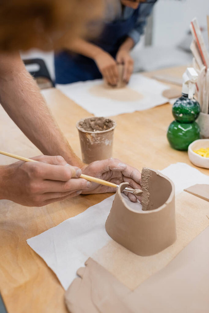 cropped view of man holding shaper while modeling clay during pottery class  - Foto, immagini