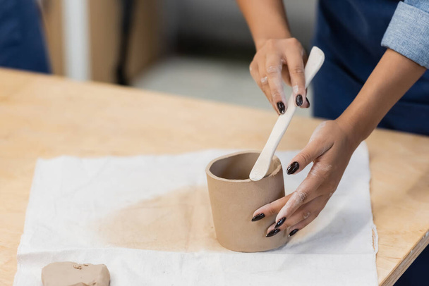 partial view african american woman with manicure modeling clay cup with shaper during pottery class  - Фото, зображення