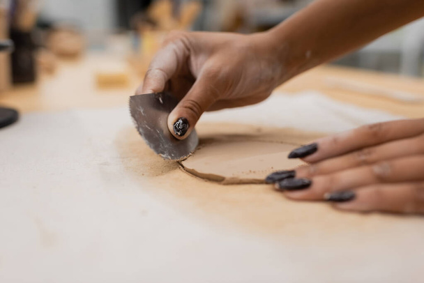 vista recortada de la mujer afroamericana con manicura que sostiene rascador de acero inoxidable mientras moldea la pieza de arcilla  - Foto, imagen
