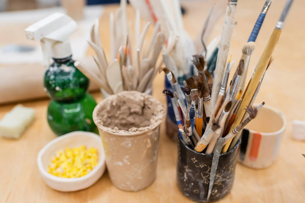 paintbrushes and pottery tools near clay cup on wooden table - Foto, Bild