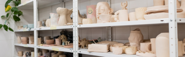 different clay sculptures near cups and bowls on shelves of pottery shop, banner - Photo, Image